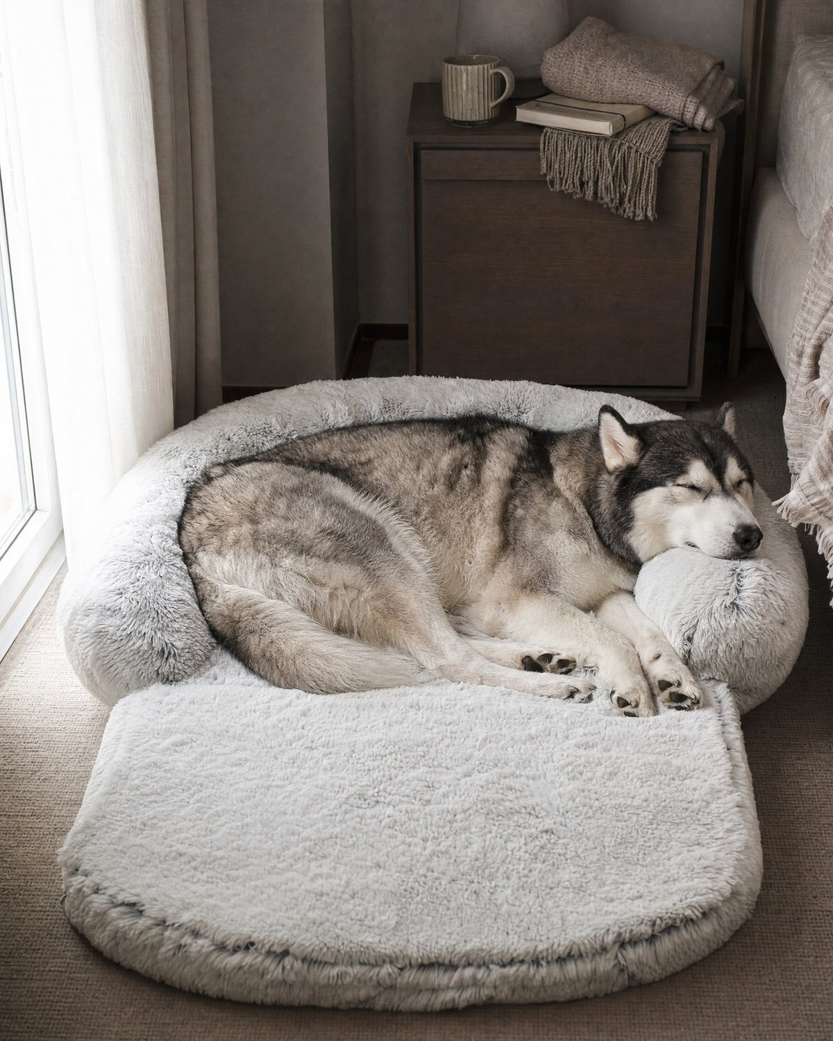 Husky resting its head on the rim of a light grey extra-large plush dog bed in a bedroom